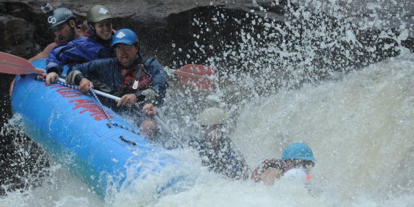 rafters holding onto the raft rope as they fall sideways down the river