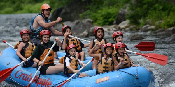 group of young rafters paddling as two girls in front link arms