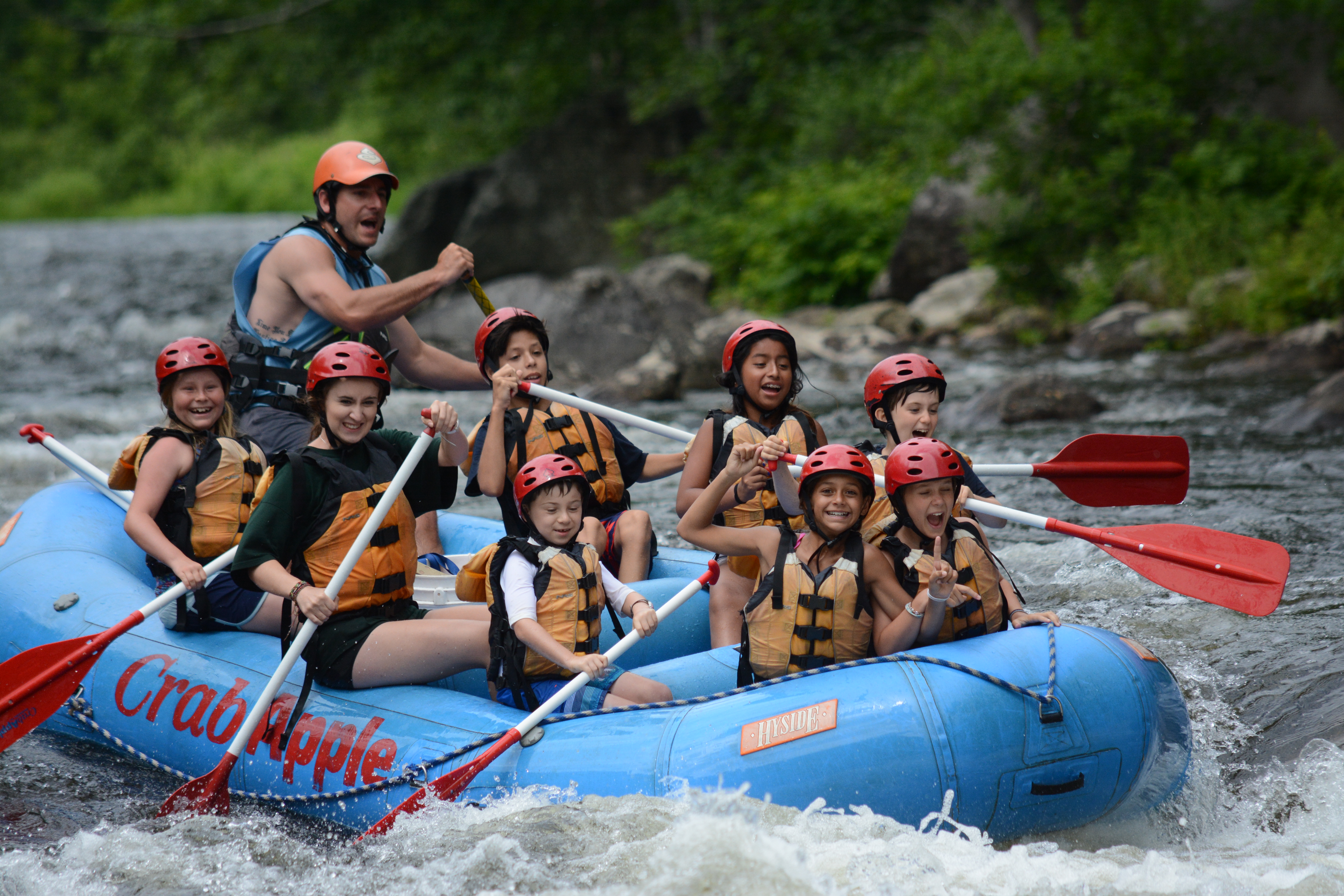 group of young rafters paddling as two girls in front link arms