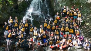 School group in rafting gear posing near a waterfall.