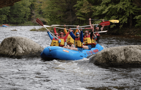 group of rafters all raising their paddles above their heads as the raft is between two large rocks