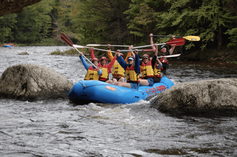 group of rafters all raising their paddles above their heads as the raft is between two large rocks