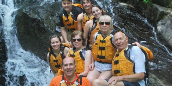 group of people with life vests posing as they smile in front of a waterfall