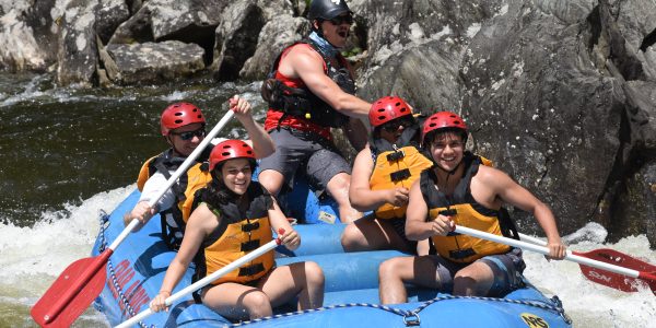 group of rafters paddling as the man in the back has his mouth his open